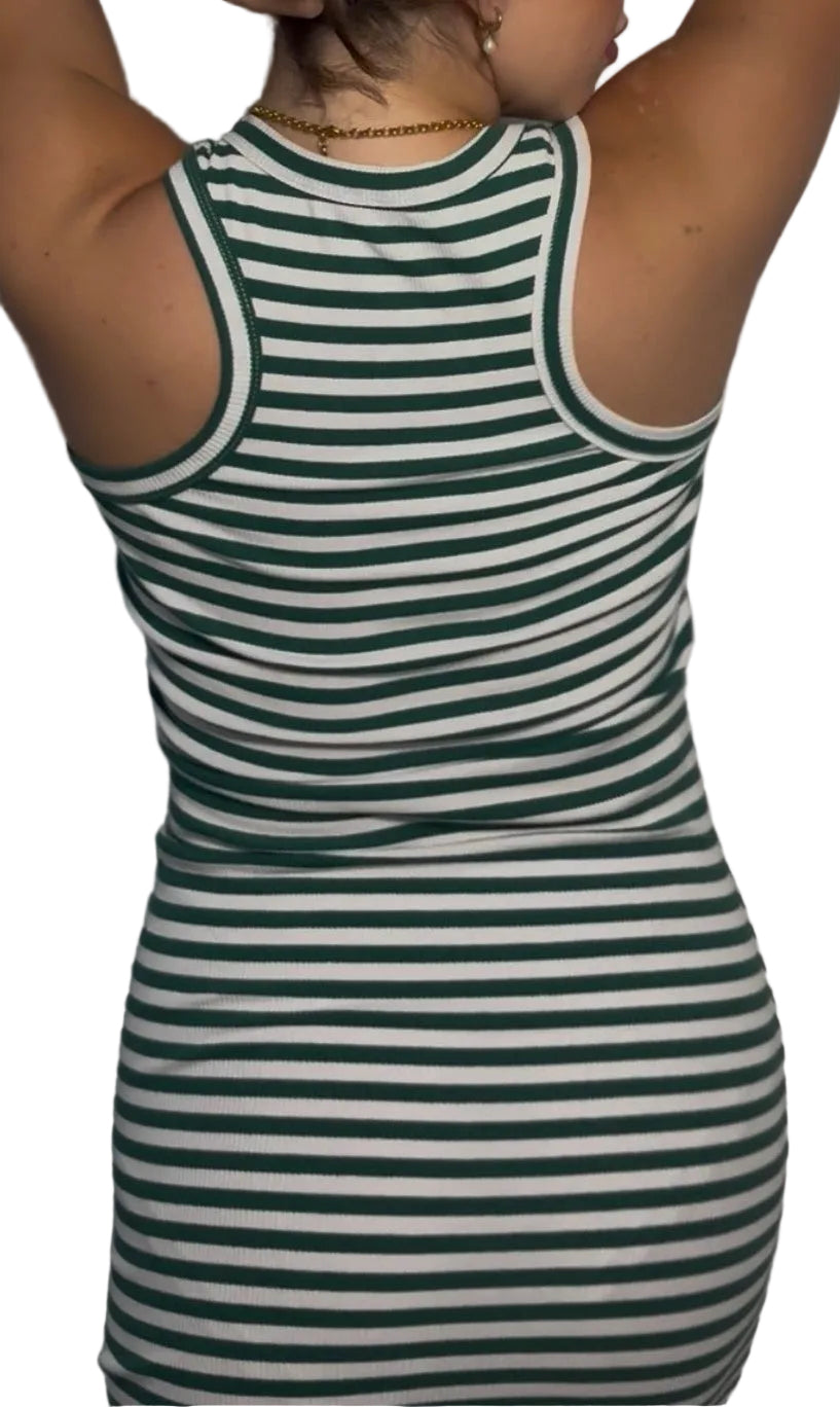 Wearing a green and white horizontally striped ribbed tank top, posing against a white textured wavy wall.